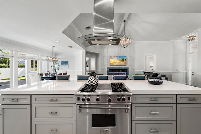 kitchen featuring high end stainless steel range, a fireplace, gray cabinetry, pendant lighting, and island exhaust hood