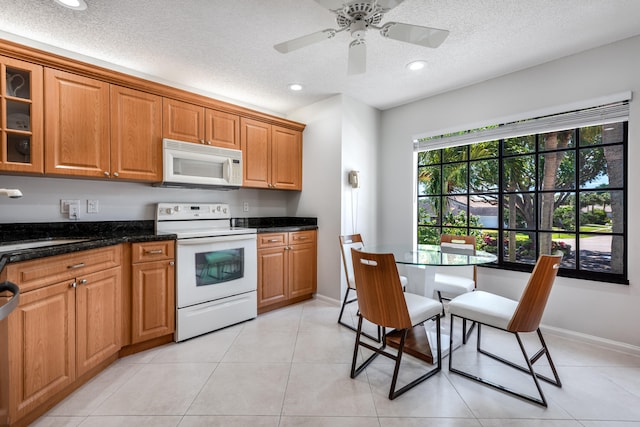 kitchen with white appliances, ceiling fan, light tile flooring, a textured ceiling, and dark stone counters