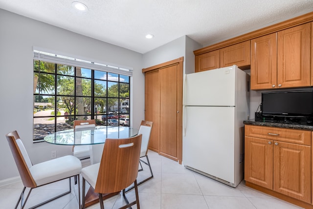 kitchen featuring white refrigerator, light tile flooring, dark stone countertops, and a textured ceiling