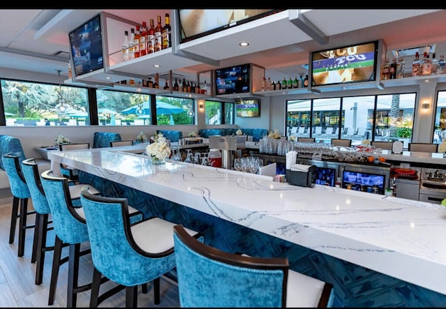 bar featuring light stone counters and light wood-type flooring