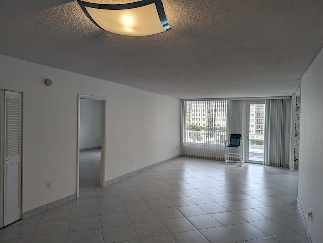 empty room with a textured ceiling, light tile patterned floors, and expansive windows