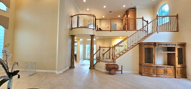 stairs featuring a towering ceiling, ornamental molding, decorative columns, and tile patterned flooring