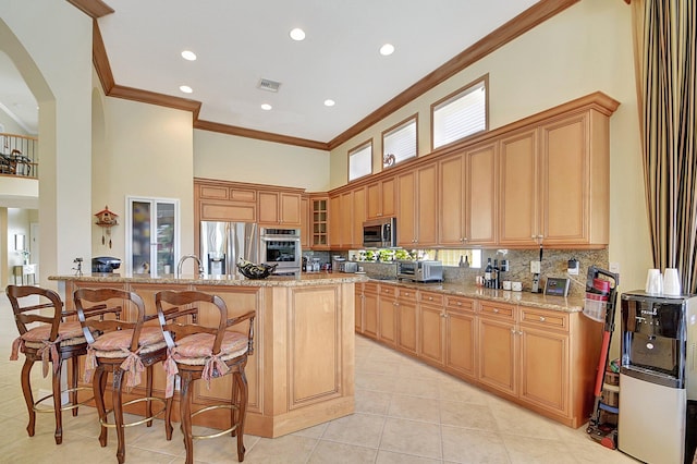 kitchen with ornamental molding, kitchen peninsula, light stone counters, and appliances with stainless steel finishes