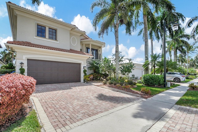 mediterranean / spanish house with an attached garage, stucco siding, decorative driveway, and a tiled roof