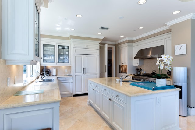 kitchen with light stone counters, wall chimney exhaust hood, backsplash, white cabinetry, and an island with sink