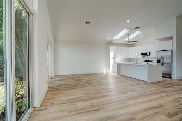 kitchen featuring a skylight, light hardwood / wood-style flooring, white cabinets, stainless steel appliances, and an island with sink