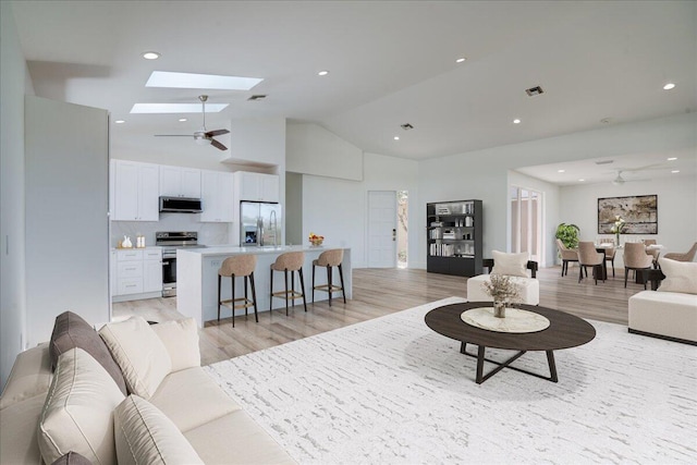 living room with a skylight, light hardwood / wood-style flooring, ceiling fan, and high vaulted ceiling