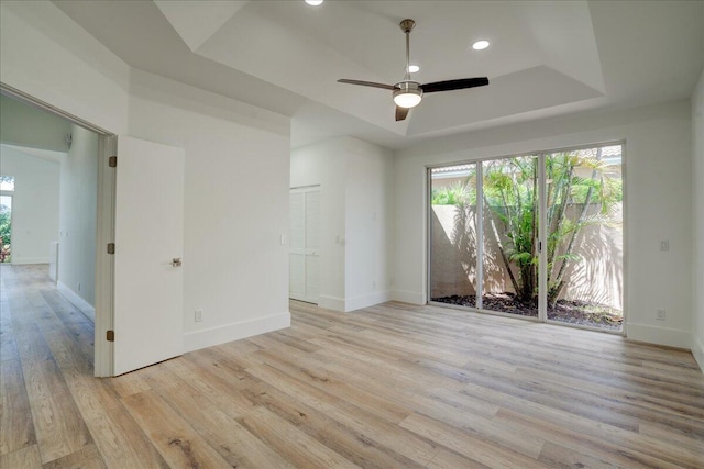 spare room with light hardwood / wood-style flooring, a raised ceiling, and ceiling fan