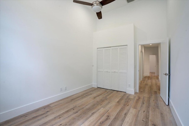 unfurnished bedroom featuring a towering ceiling, ceiling fan, a closet, and light wood-type flooring