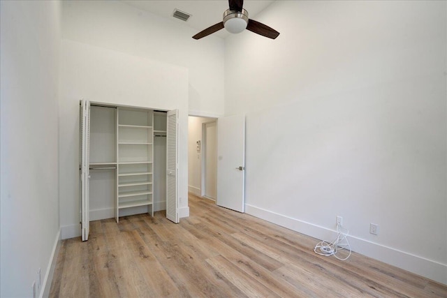 unfurnished bedroom with a closet, light hardwood / wood-style flooring, ceiling fan, and a high ceiling