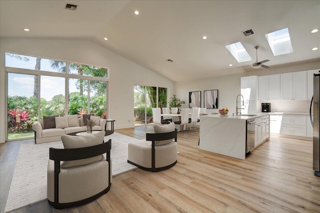 living room featuring high vaulted ceiling, light hardwood / wood-style flooring, sink, a skylight, and ceiling fan