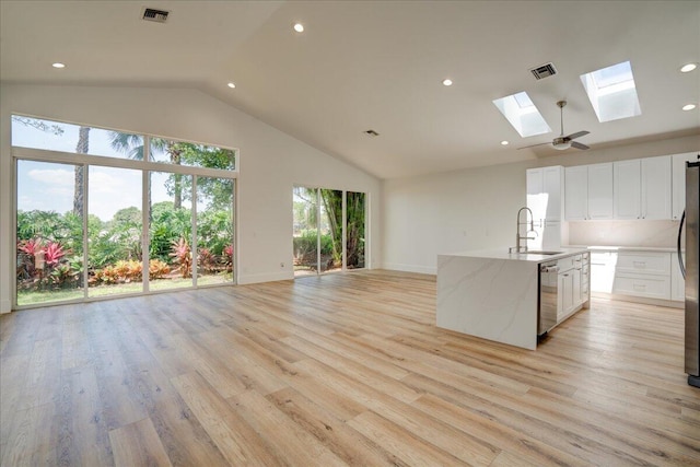 kitchen featuring light hardwood / wood-style floors, white cabinets, a kitchen island with sink, light stone counters, and a skylight