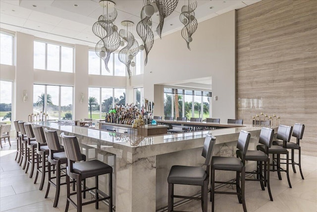 kitchen with a towering ceiling, a kitchen bar, light stone counters, a notable chandelier, and light tile floors