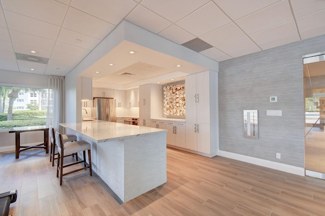 kitchen with white cabinets, stainless steel fridge, light stone counters, and light wood-type flooring