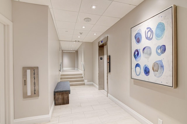 corridor featuring a paneled ceiling, light tile patterned floors, and elevator