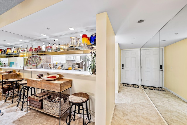 bar with light tile patterned floors, white cabinetry, and backsplash