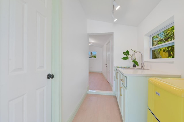 corridor with rail lighting, light hardwood / wood-style flooring, sink, and vaulted ceiling