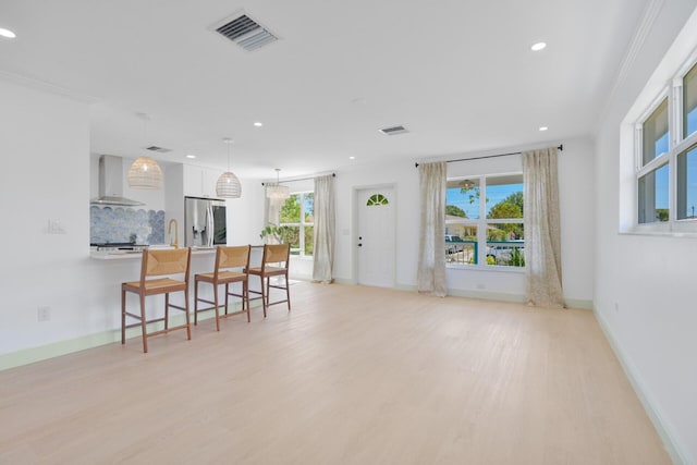 interior space with wall chimney range hood, white cabinetry, hanging light fixtures, light hardwood / wood-style flooring, and stainless steel refrigerator with ice dispenser