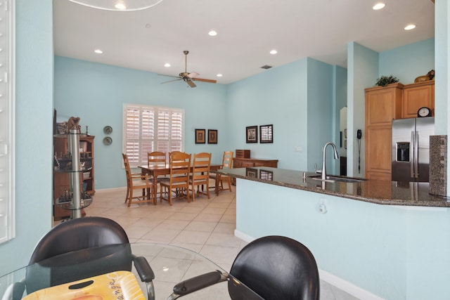 kitchen featuring stainless steel fridge with ice dispenser, ceiling fan, light tile flooring, dark stone countertops, and sink