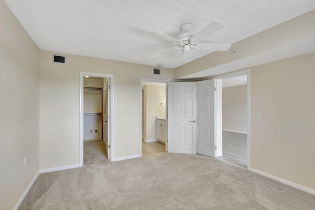 unfurnished bedroom featuring light carpet, a closet, ensuite bath, ceiling fan, and a walk in closet