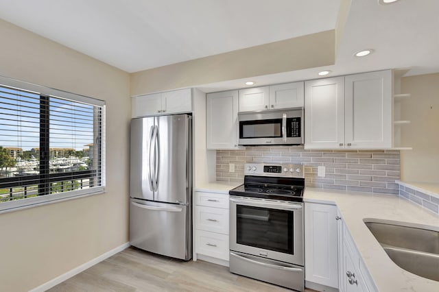 kitchen with backsplash, light wood-type flooring, white cabinetry, stainless steel appliances, and light stone countertops