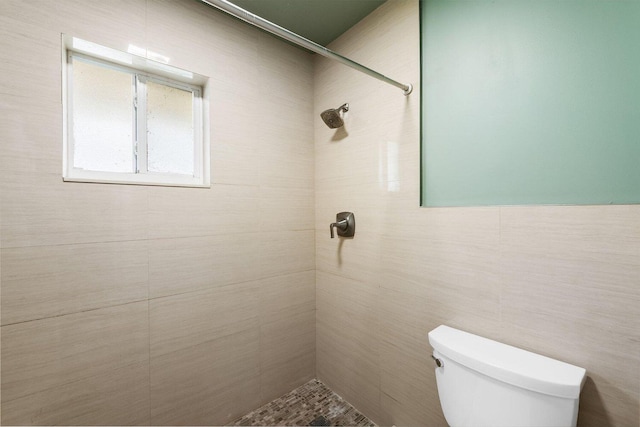 bathroom with a tile shower, toilet, and tile walls