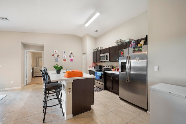 kitchen featuring light tile floors, a kitchen island, stainless steel appliances, vaulted ceiling, and a kitchen breakfast bar