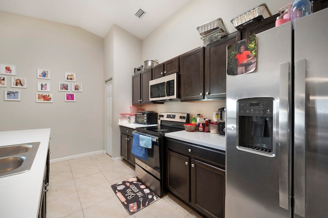 kitchen featuring appliances with stainless steel finishes, dark brown cabinets, light tile floors, and vaulted ceiling