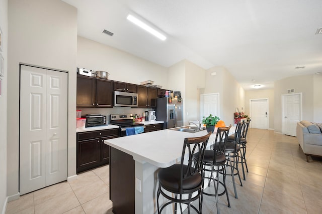 kitchen with dark brown cabinetry, light tile floors, a kitchen bar, stainless steel appliances, and a center island with sink