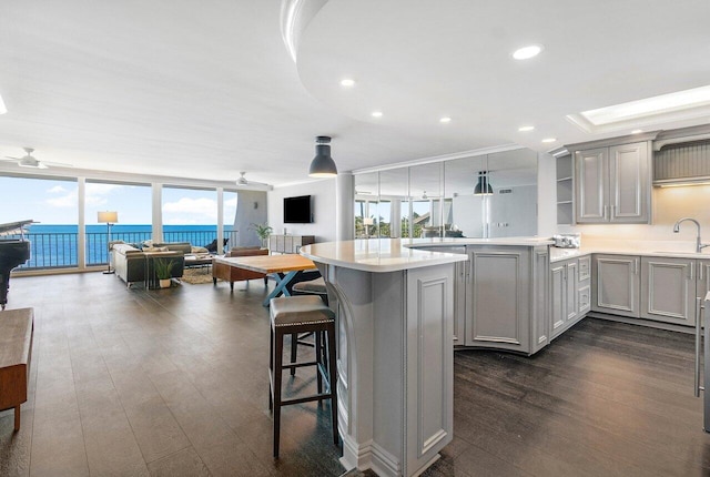 kitchen with a kitchen breakfast bar, gray cabinets, dark wood-type flooring, kitchen peninsula, and sink