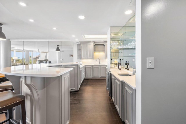 kitchen featuring hanging light fixtures, gray cabinets, dark hardwood / wood-style flooring, sink, and a breakfast bar area