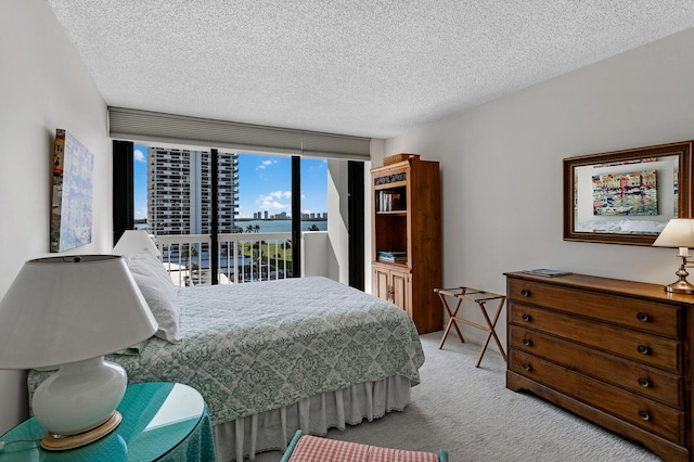 carpeted bedroom featuring a textured ceiling, a wall of windows, a water view, and access to outside