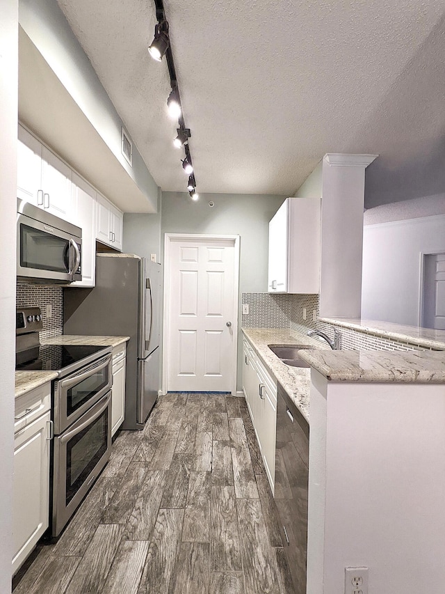 kitchen with appliances with stainless steel finishes, dark hardwood / wood-style floors, white cabinetry, light stone counters, and kitchen peninsula