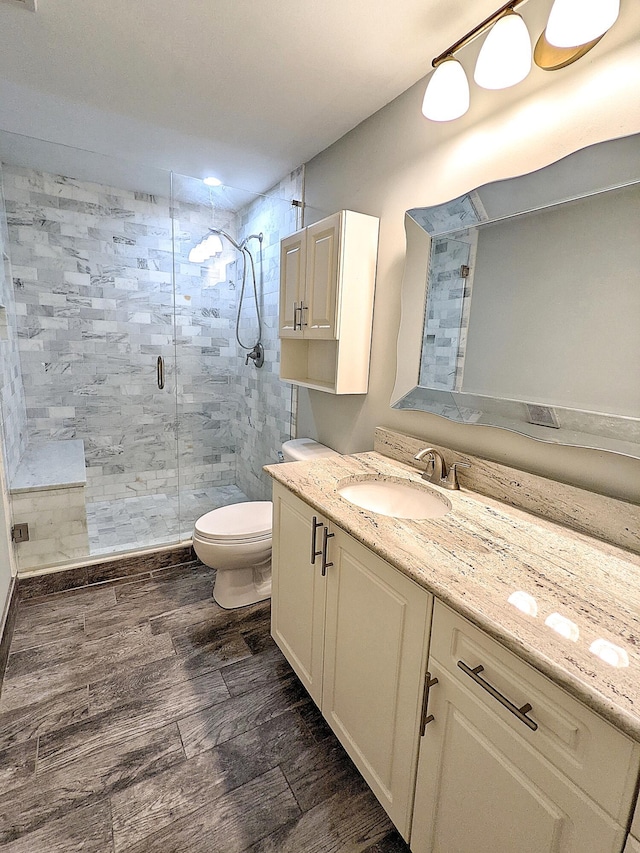 bathroom featuring wood-type flooring, toilet, a shower with door, and vanity