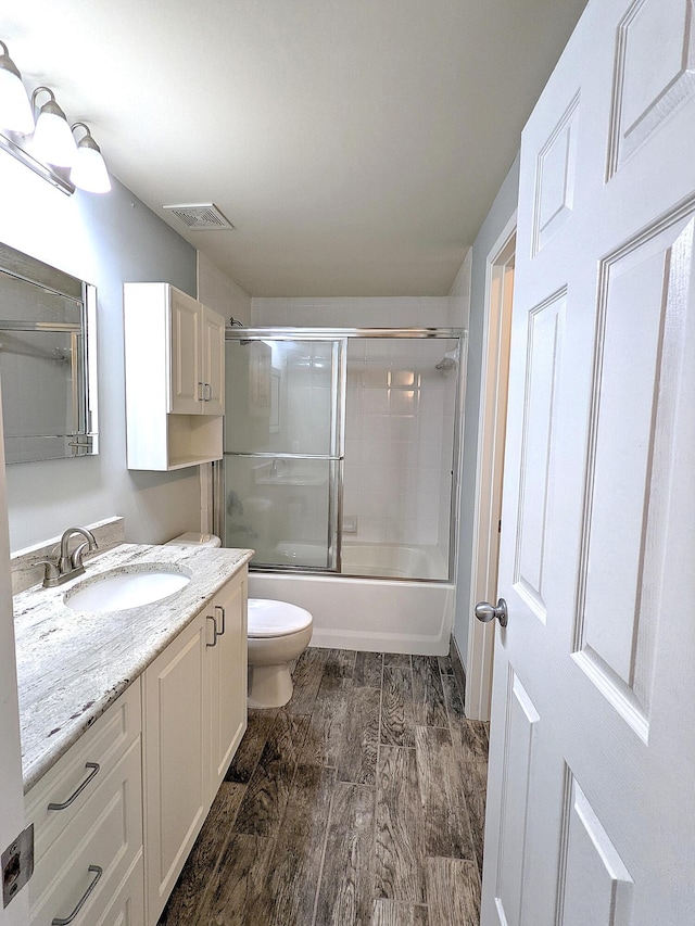 full bathroom featuring vanity, wood-type flooring, shower / bath combination with glass door, and toilet