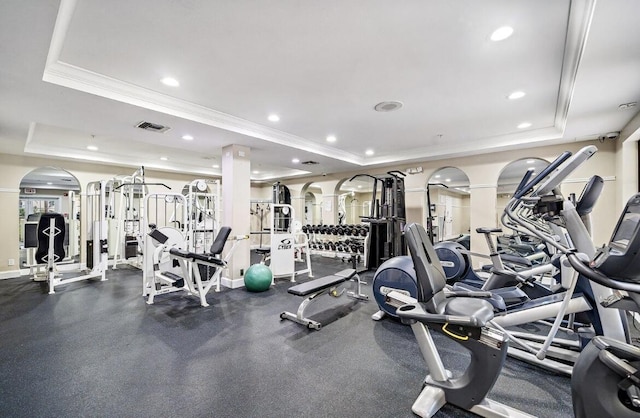 gym with ornate columns, ornamental molding, and a tray ceiling