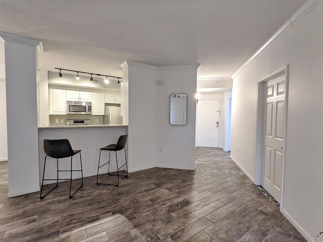 kitchen with appliances with stainless steel finishes, white cabinetry, dark hardwood / wood-style flooring, a kitchen bar, and kitchen peninsula