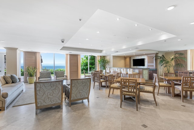 dining area with a water view, a raised ceiling, floor to ceiling windows, and light tile floors