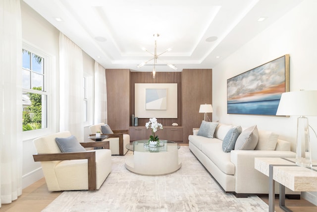 living room with a chandelier, a raised ceiling, and light hardwood / wood-style flooring