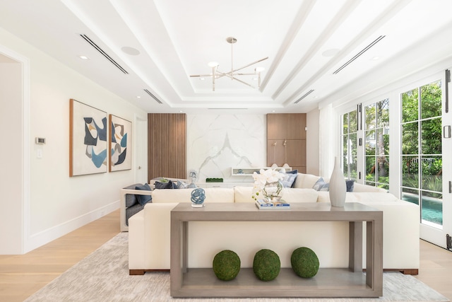 living room featuring a chandelier, a raised ceiling, and light wood-type flooring