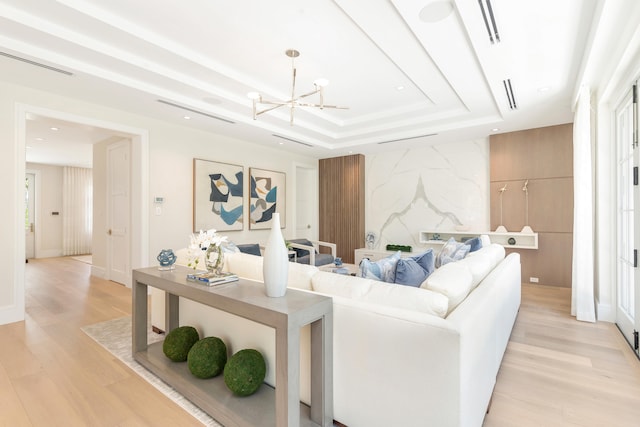 living room with light hardwood / wood-style floors, a notable chandelier, and a raised ceiling