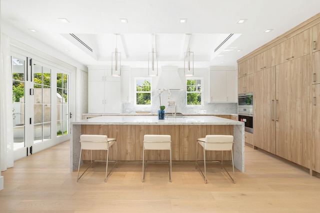 kitchen with light hardwood / wood-style flooring, hanging light fixtures, a large island, and white cabinets