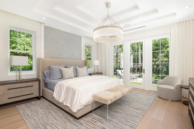 bedroom featuring a chandelier, access to outside, a tray ceiling, and light hardwood / wood-style floors