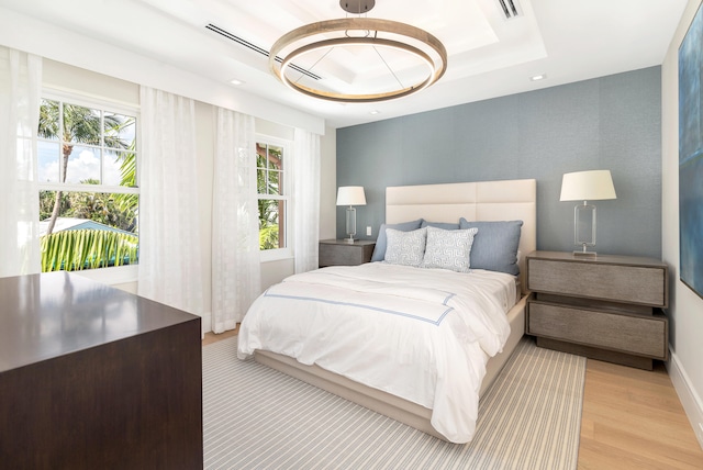 bedroom featuring a notable chandelier, light wood-type flooring, and a tray ceiling