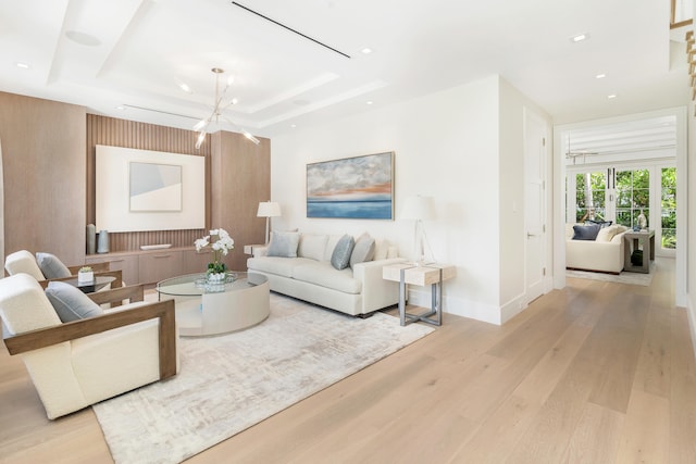 living room featuring a tray ceiling, light wood-type flooring, and a chandelier