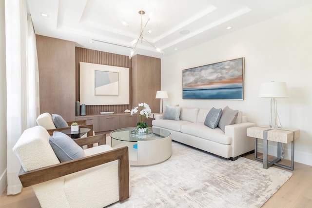 living room with light wood-type flooring, a tray ceiling, and a notable chandelier