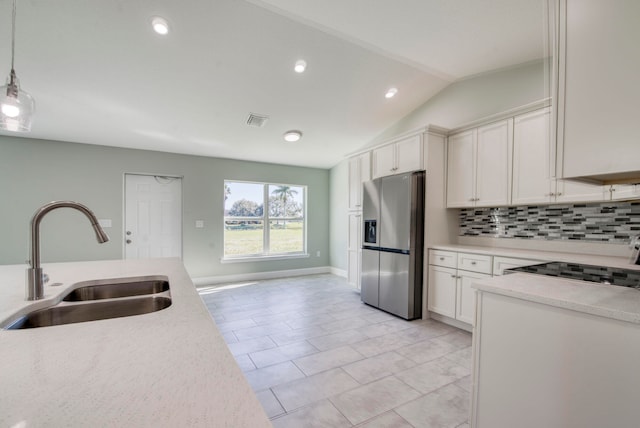 kitchen featuring stainless steel refrigerator with ice dispenser, vaulted ceiling, sink, pendant lighting, and white cabinets