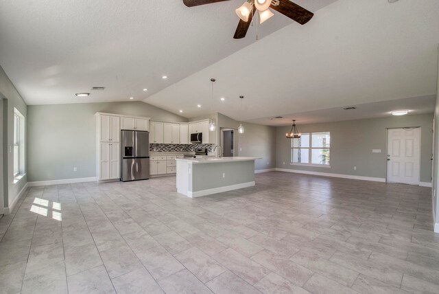 kitchen featuring white cabinets, vaulted ceiling, an island with sink, decorative light fixtures, and stainless steel appliances