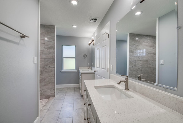 bathroom with tile patterned flooring, vanity, a textured ceiling, and tiled shower