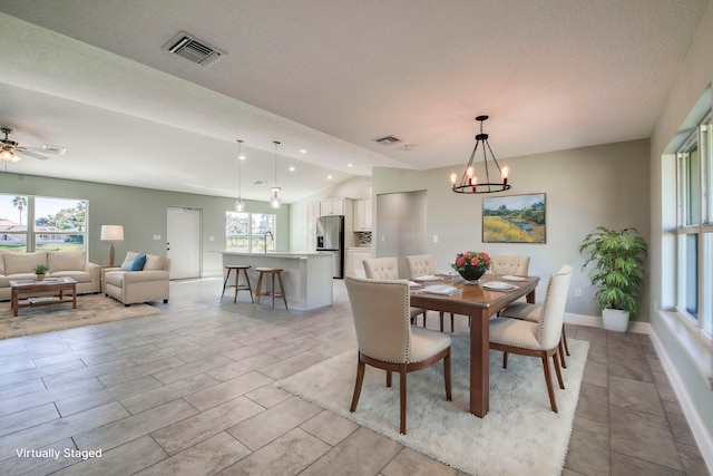 dining space featuring ceiling fan with notable chandelier, a textured ceiling, a wealth of natural light, and vaulted ceiling